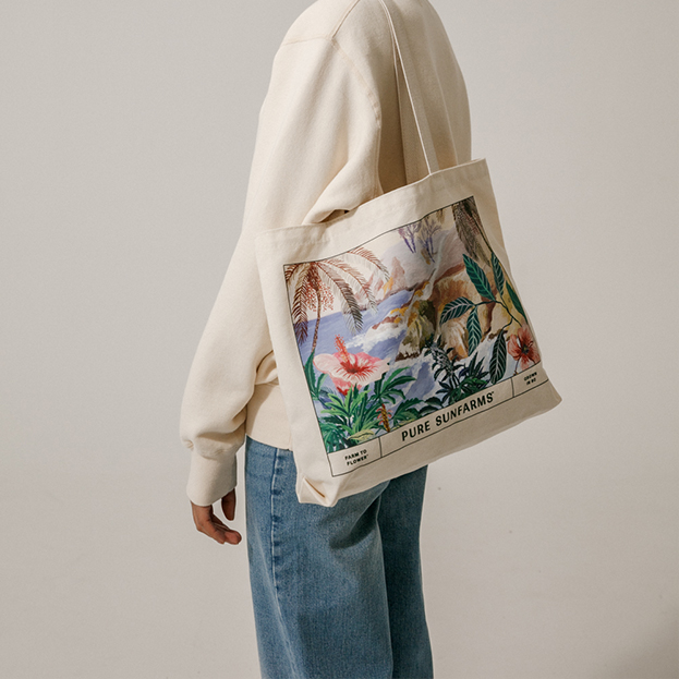 Model wearing beige crewneck with Cannabis plant embroidery and carrying tote bag with illustration.