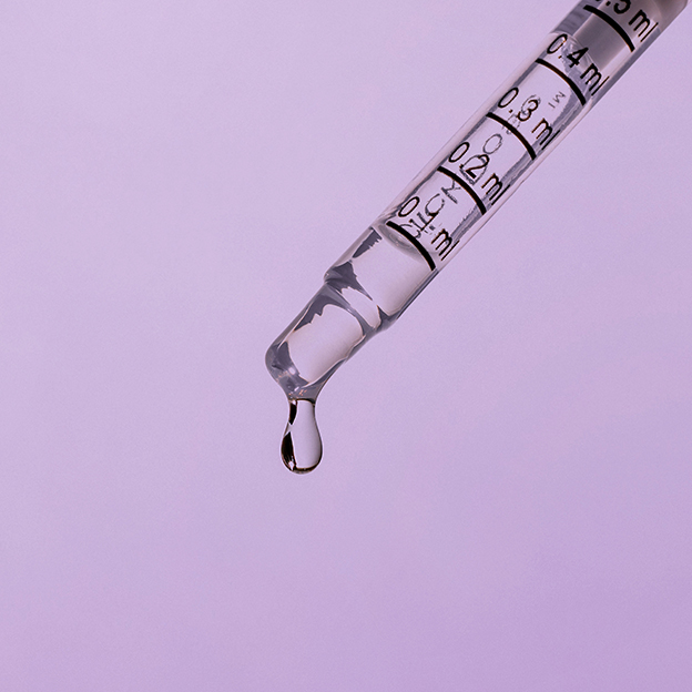 syringe with oil dripping from the end on a purple background