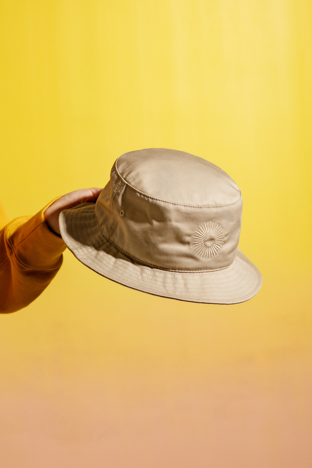 hand holding classic bucket hat on yellow backdrop