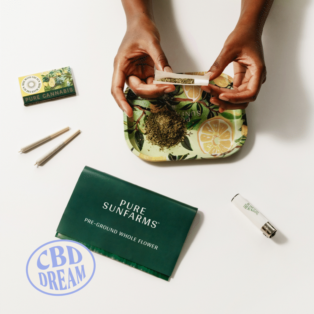 Hands rolling a joint with CBD Dream preground. Tray, packaging and paper in the picture. 