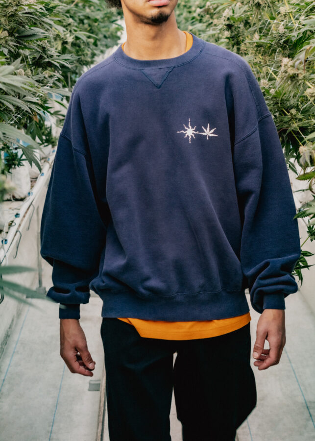 Model wearing blue crewneck in the greenhouse