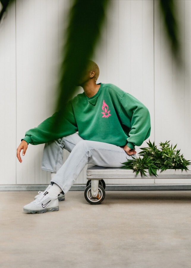 Model wearing green crewneck greenhouse with cannabis plants